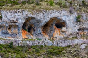 Explore intricate rock formations and natural caves carved into a rugged cliffside, showcasing geological wonders.