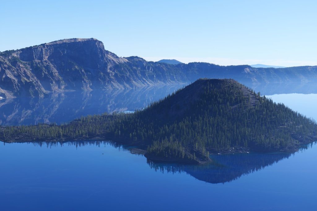 A stunning view of a mountain and forested island reflecting in the calm waters of Crater Lake.