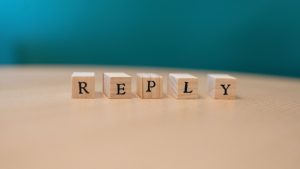 Close-up of wooden blocks spelling 'REPLY' on a table with teal background.